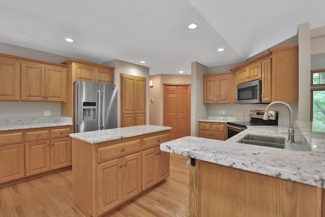 kitchen featuring light stone countertops, appliances with stainless steel finishes, vaulted ceiling, sink, and light hardwood / wood-style floors