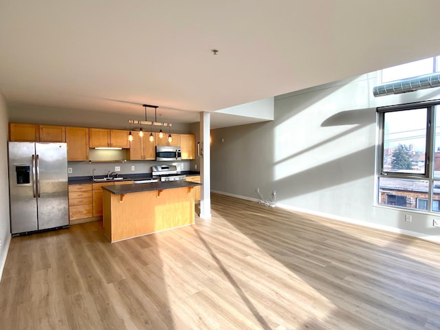 kitchen featuring sink, appliances with stainless steel finishes, decorative light fixtures, a kitchen island, and a breakfast bar area