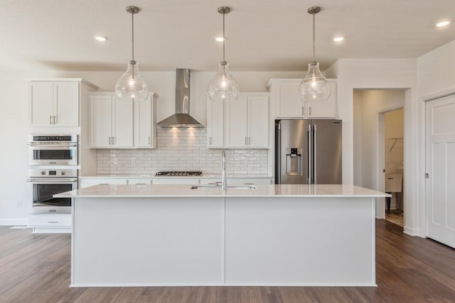 kitchen with white cabinetry, sink, stainless steel appliances, wall chimney range hood, and an island with sink