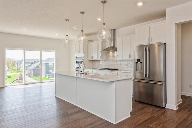 kitchen featuring a center island with sink, white cabinets, wall chimney range hood, and appliances with stainless steel finishes