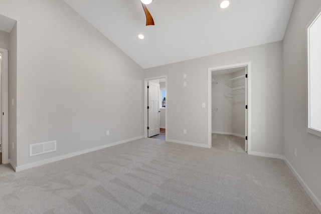 unfurnished bedroom with lofted ceiling, ceiling fan, a walk in closet, light colored carpet, and a closet