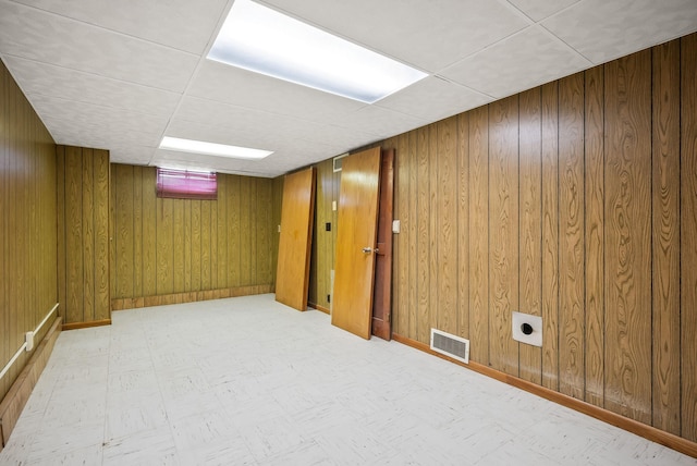 finished below grade area featuring a paneled ceiling, wooden walls, visible vents, and tile patterned floors