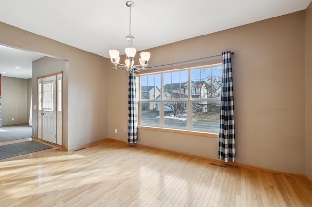 empty room with light hardwood / wood-style flooring and a notable chandelier