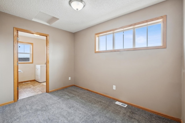 carpeted spare room with a healthy amount of sunlight, a textured ceiling, and washer / clothes dryer