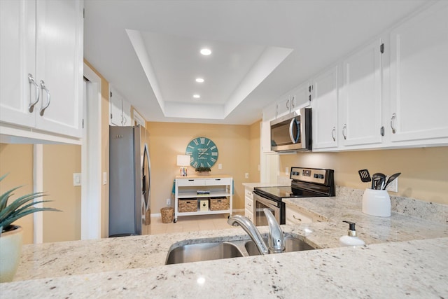 kitchen featuring light stone countertops, stainless steel appliances, a raised ceiling, sink, and white cabinetry