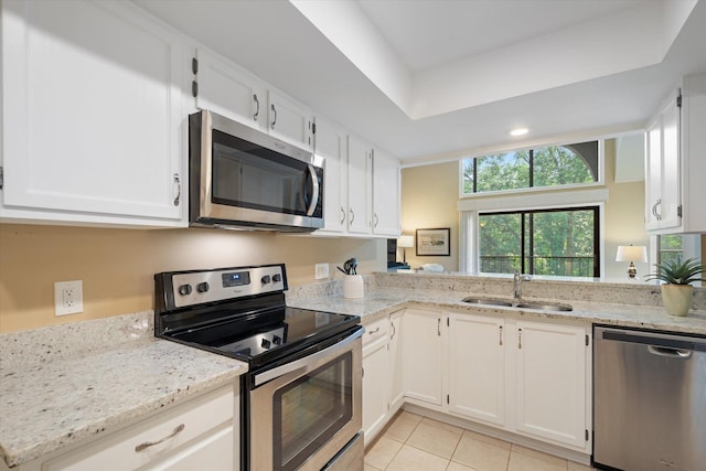 kitchen with appliances with stainless steel finishes, light stone counters, sink, light tile patterned floors, and white cabinetry