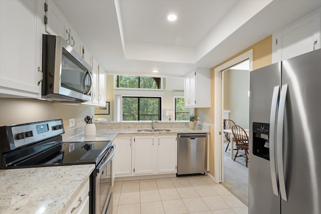 kitchen featuring appliances with stainless steel finishes, light stone counters, a tray ceiling, sink, and white cabinets