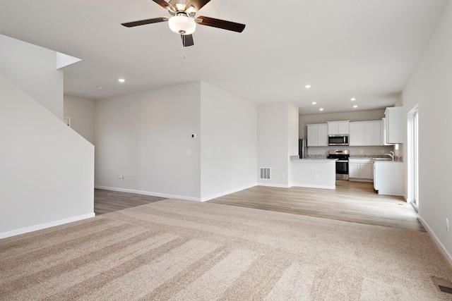 unfurnished living room with ceiling fan, sink, and light carpet