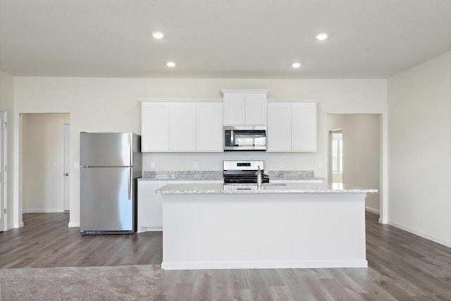 kitchen with hardwood / wood-style floors, a center island with sink, appliances with stainless steel finishes, light stone counters, and white cabinetry