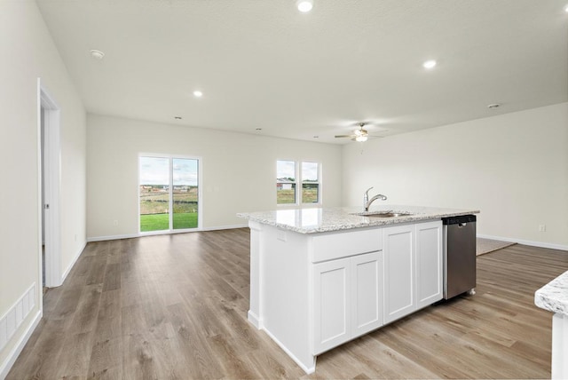 kitchen with light stone counters, stainless steel dishwasher, a kitchen island with sink, sink, and white cabinetry