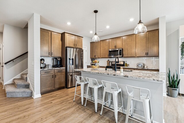 14592 Twin Lakes Cir, Burnsville, MN 55306 - kitchen featuring stainless steel appliances, light wood-style flooring, a center island with sink, tasteful backsplash, and a breakfast bar