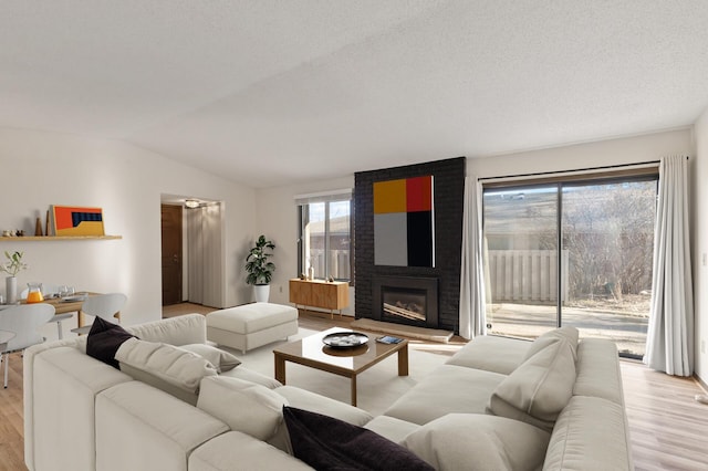 living room with a textured ceiling, light wood-type flooring, lofted ceiling, and a brick fireplace