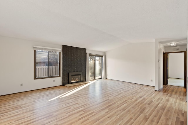 unfurnished living room featuring light wood-type flooring, lofted ceiling, a textured ceiling, and a brick fireplace