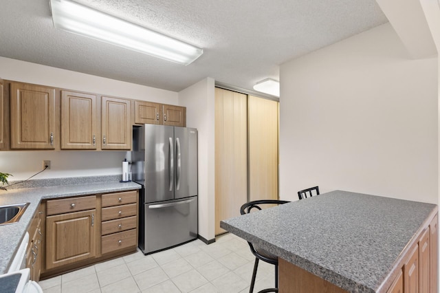 kitchen featuring a kitchen bar, a textured ceiling, sink, light tile patterned floors, and stainless steel refrigerator