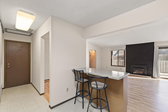 kitchen with a textured ceiling, kitchen peninsula, a breakfast bar area, and a brick fireplace