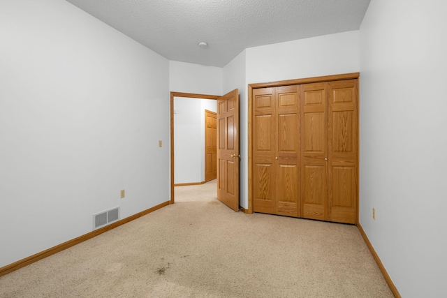 unfurnished bedroom with light colored carpet, a closet, and a textured ceiling