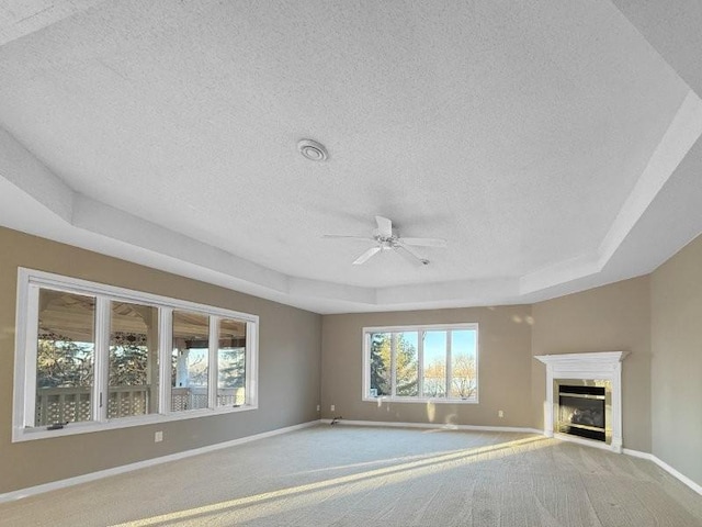 unfurnished living room featuring carpet, ceiling fan, a textured ceiling, and a tray ceiling