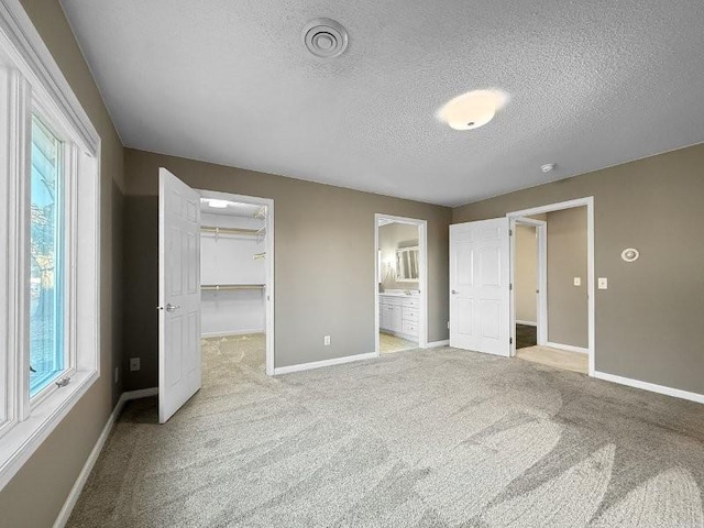 unfurnished bedroom featuring ensuite bath, a walk in closet, light carpet, and a textured ceiling