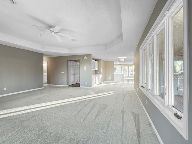 unfurnished living room with a tray ceiling, ceiling fan, and light carpet