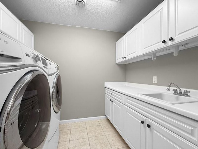 laundry area featuring cabinets, a textured ceiling, sink, light tile patterned floors, and separate washer and dryer