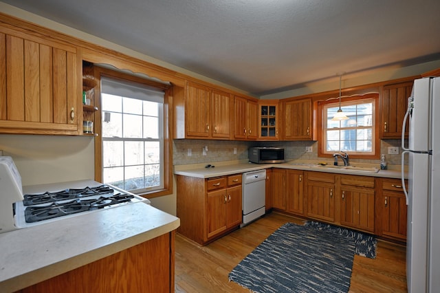 kitchen featuring sink, light hardwood / wood-style flooring, white appliances, decorative light fixtures, and decorative backsplash