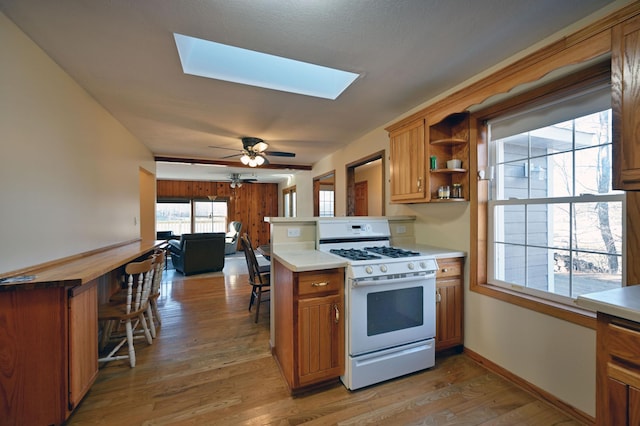 kitchen with a skylight, ceiling fan, white range with gas stovetop, kitchen peninsula, and wood-type flooring