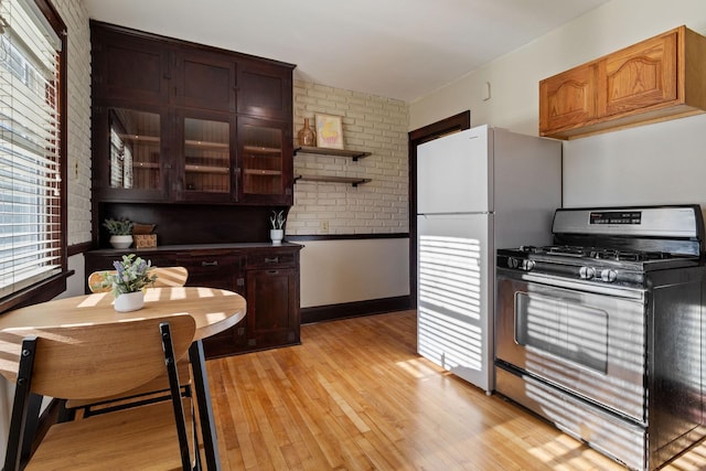 kitchen featuring light hardwood / wood-style floors, brick wall, stainless steel gas range, dark brown cabinets, and white fridge