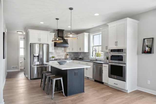 kitchen featuring a center island, stainless steel appliances, decorative light fixtures, white cabinets, and custom exhaust hood