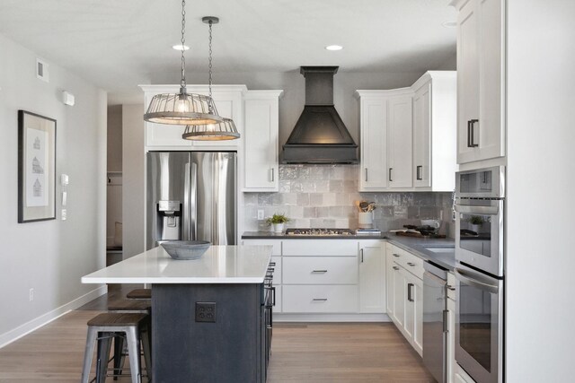 kitchen with hanging light fixtures, backsplash, white cabinets, custom exhaust hood, and appliances with stainless steel finishes