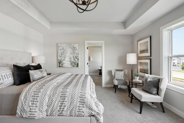 bedroom with ensuite bath, an inviting chandelier, light colored carpet, and a tray ceiling