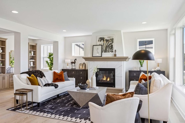 living room featuring light hardwood / wood-style flooring, built in features, a healthy amount of sunlight, and a premium fireplace