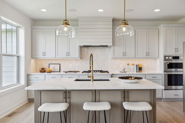 kitchen featuring stainless steel appliances, light stone countertops, light hardwood / wood-style flooring, and a kitchen island with sink