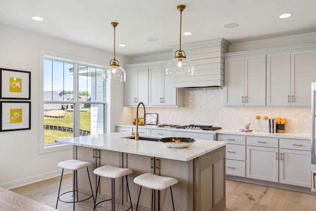 kitchen featuring light stone counters, a center island with sink, and light hardwood / wood-style flooring