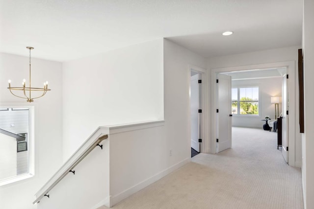 hallway with light carpet and a chandelier