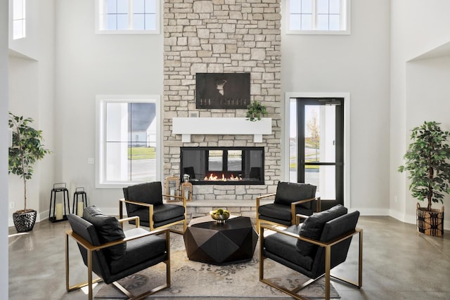 living room with concrete flooring, a high ceiling, and a stone fireplace