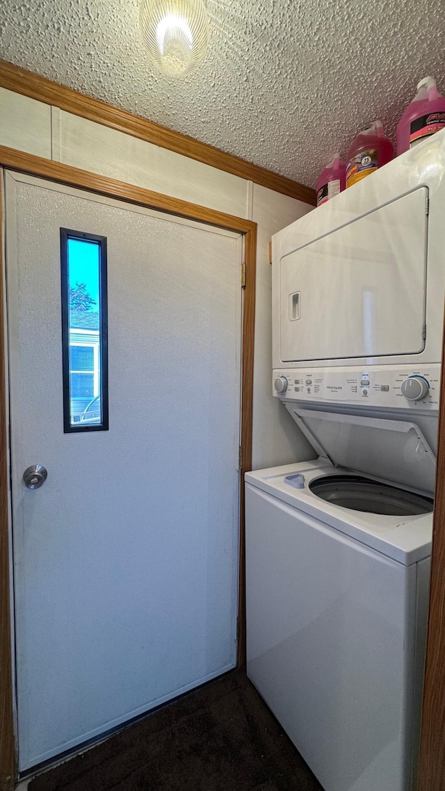 clothes washing area with ornamental molding, a textured ceiling, and stacked washer and clothes dryer