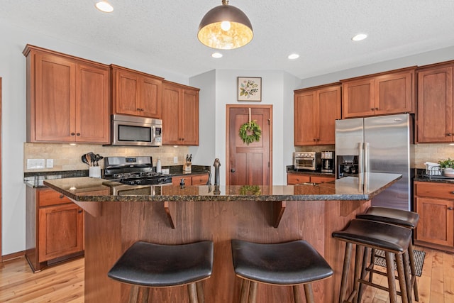 kitchen with a kitchen bar, light wood-type flooring, a kitchen island with sink, stainless steel appliances, and dark stone counters