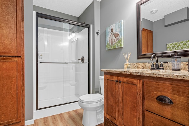 bathroom with a textured ceiling, toilet, hardwood / wood-style floors, and an enclosed shower