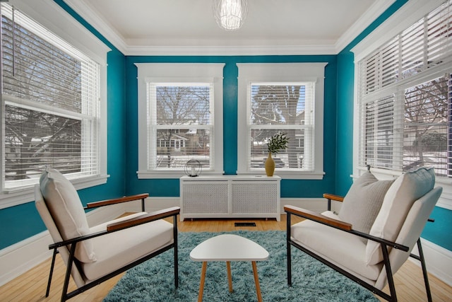 living area with a healthy amount of sunlight, crown molding, radiator, and light hardwood / wood-style flooring