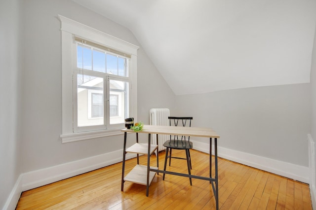 office area featuring light wood-type flooring, vaulted ceiling, and radiator