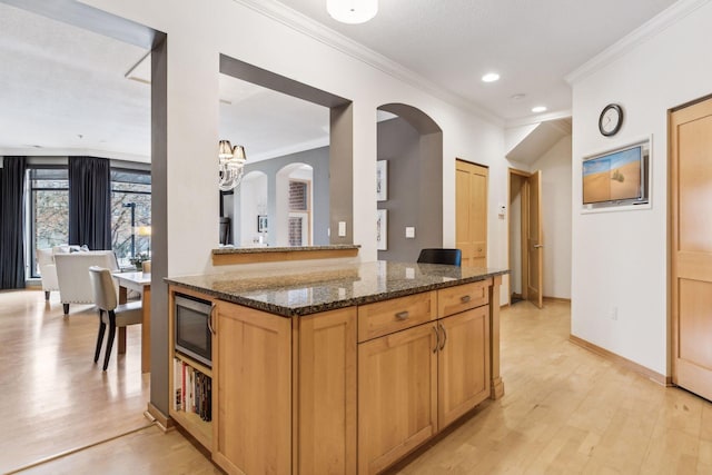 kitchen with stainless steel microwave, light hardwood / wood-style flooring, dark stone counters, and kitchen peninsula