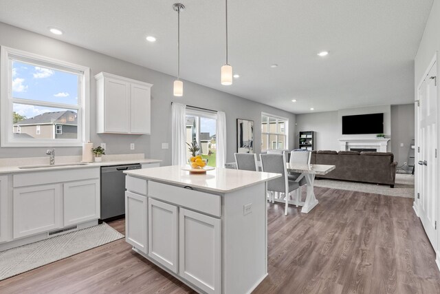 kitchen with white cabinets, sink, hanging light fixtures, stainless steel dishwasher, and light wood-type flooring