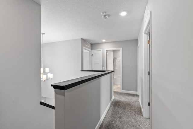 corridor with dark colored carpet, a textured ceiling, and an inviting chandelier