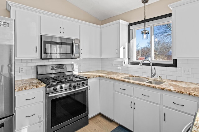 kitchen featuring appliances with stainless steel finishes, white cabinetry, lofted ceiling, and sink