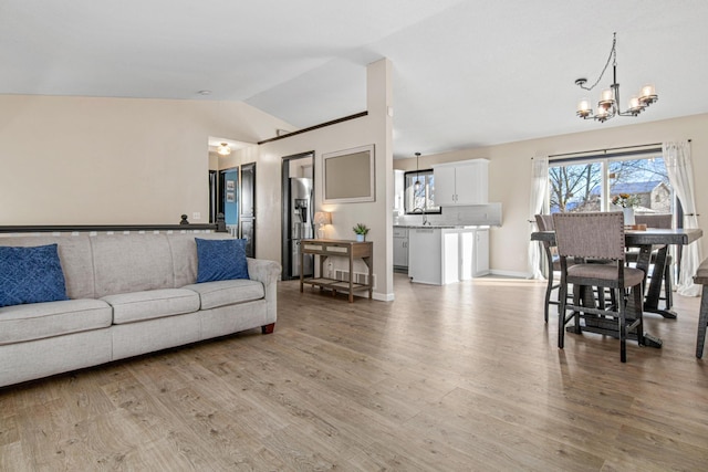 living room featuring sink, light wood-type flooring, lofted ceiling, and a chandelier