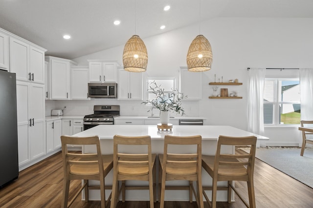 kitchen featuring white cabinets, vaulted ceiling, appliances with stainless steel finishes, decorative light fixtures, and a kitchen island