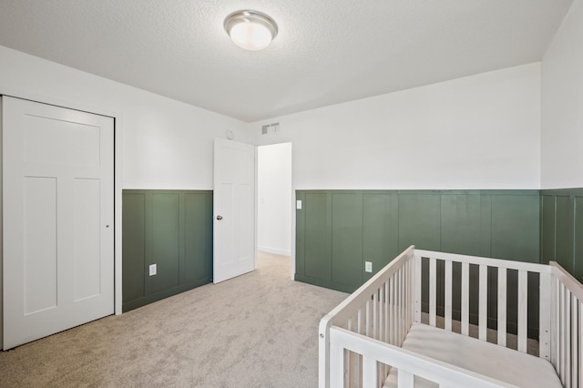 carpeted bedroom featuring a nursery area and a textured ceiling