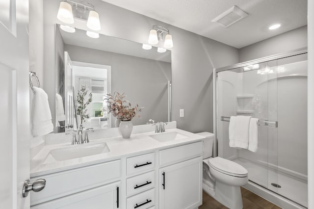 bathroom featuring vanity, toilet, a shower with shower door, and a textured ceiling