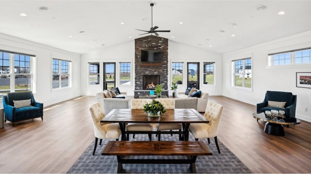 dining room with ceiling fan, a stone fireplace, and wood-type flooring