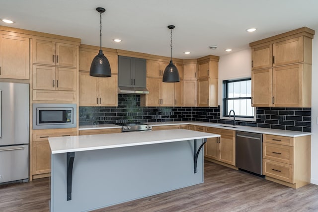 kitchen with appliances with stainless steel finishes, sink, wood-type flooring, a kitchen island, and hanging light fixtures